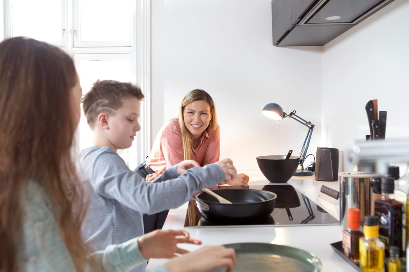 Una madre sonriendo mientras sus hijos cocinan juntos en la cocina